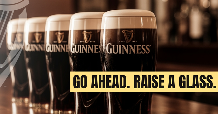 Five perfect pints of Guinness lined up on a bar. Half a Guinness harp logo faded in the left corner. Headline: "Go Ahead. Raise a Glass"
